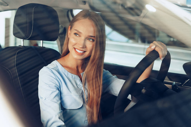 Attractive young woman sitting in new car in showroom - Φωτογραφία, εικόνα