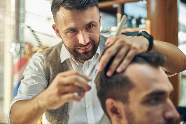Cheerful hair-groomer giving his client a haircut - Foto, Imagen