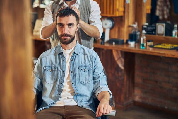 Brunette man looking serious during hair styling - Foto, afbeelding