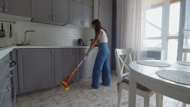 Genç ve güzel bir kadın mutfakta yerleri paspasla temizliyor. - Video, Çekim