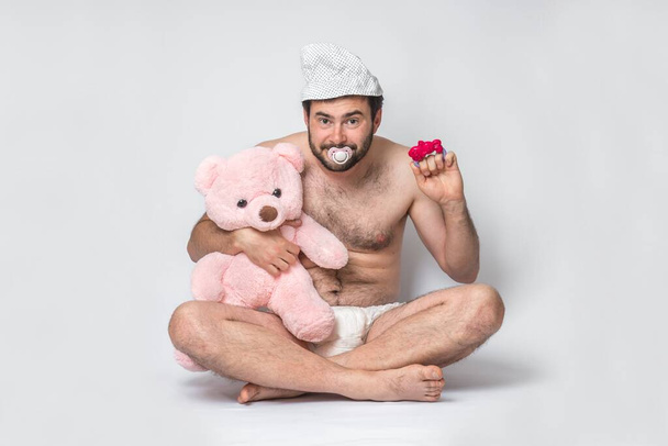 Infant adult man with pacifier in diaper holding pink teddy bear. Big baby. - Фото, изображение