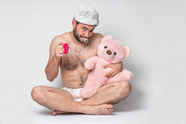 Homem adulto infantil com chupeta em fralda segurando ursinho de pelúcia rosa. Grande bebê. - Foto, Imagem