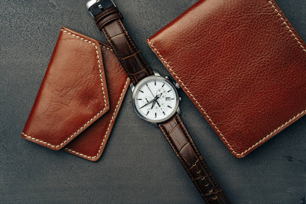 Male watch and leather wallet on dark grey surface - 写真・画像