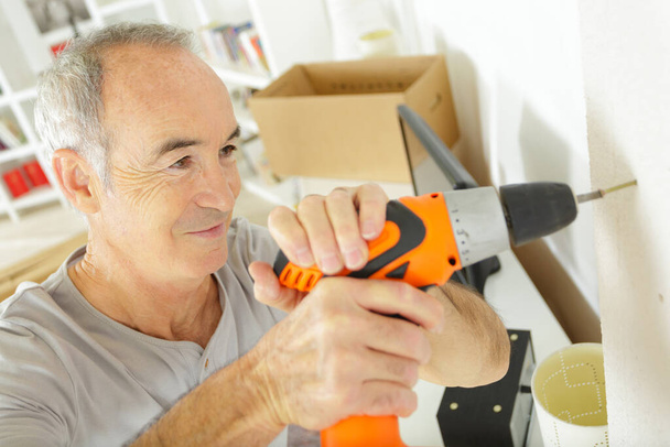 senior man using cordless screwdriver in the home - Фото, изображение