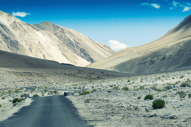 A concrete road towards beautiful rocky mountains and blue sky with peaks of Himalaya, Leh, Ladakh, Jammu and Kashmir, India - Photo, Image