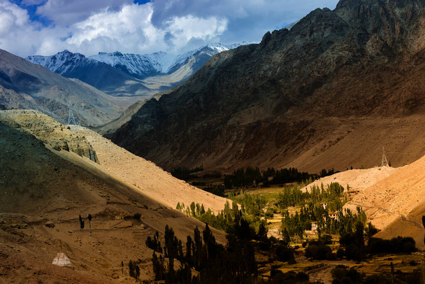 Spelen van licht en schaduw op prachtige rotsachtige landschap van Ladakh met groene vallei in het midden, Jammu en Kasjmir, Leh, India. Ladakh is een toeristische attractie van over de hele wereld. - Foto, afbeelding