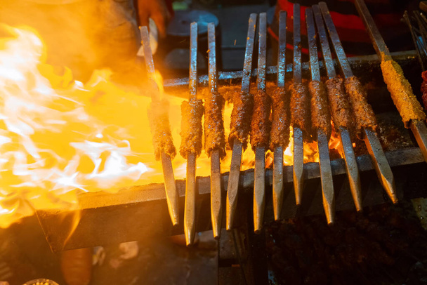 Пряный цыпленок Sekh kababs жарят на гриле в барбекю с металлическими шампурами, вечером для продажи в качестве уличной еды на рынке Старого Дели. Он знаменит пряными индийскими не вегетарианскими уличными блюдами. - Фото, изображение