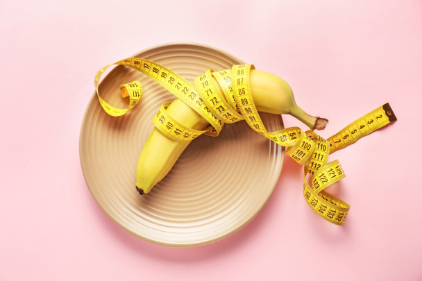 Plate with measuring tape and banana on color background. Concept of anorexia - Φωτογραφία, εικόνα