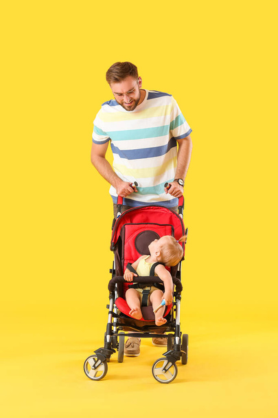Father and his cute baby in stroller on color background - Photo, Image
