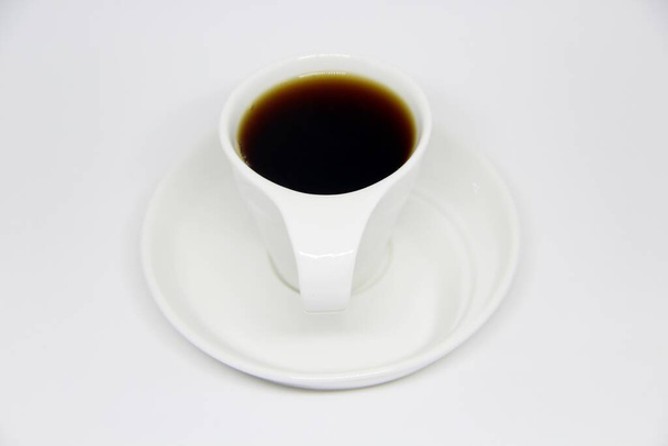 Blick auf eine volle Kaffeetasse auf einer Untertasse vor weißem Hintergrund  - Foto, Bild