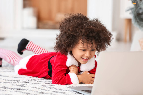 Roztomilé afroamerické dívka v kostýmu Santa a s notebookem doma na Štědrý večer - Fotografie, Obrázek