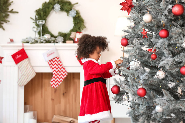 Schattig Afrikaans-Amerikaans meisje in Santa kostuum versieren kerstboom thuis - Foto, afbeelding