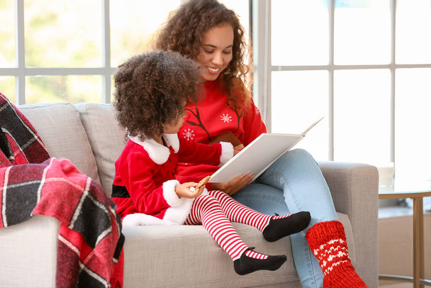 Cute African-American girl and her mother reading book at home on Christmas eve - Фото, зображення