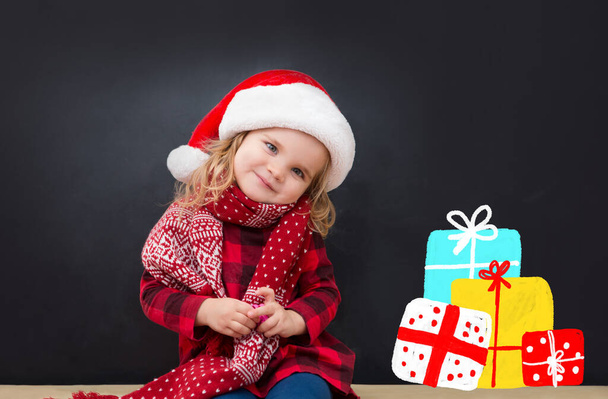 Happy child in Santa red hat with draw Christmas gifts and Christmas tree on blackboard. Christmas holiday concept. - Fotografie, Obrázek