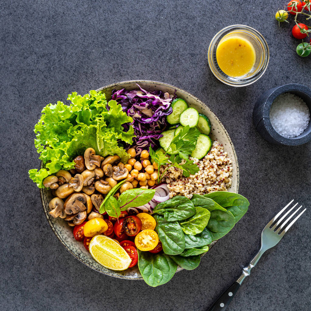 Quinoa, mushrooms, lettuce, red cabbage, spinach, cucumbers, tomatoes, a bowl of Buddha on a dark background, top view. Delicious balanced nutrition concept - Photo, Image