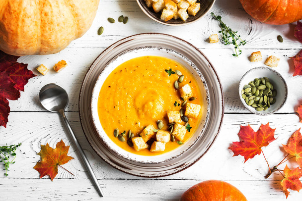 Pumpkin soup and organic pumpkins on white wooden table, top view. Seasonal autumn food - Spicy pumpkin and carrot soup. - Photo, image