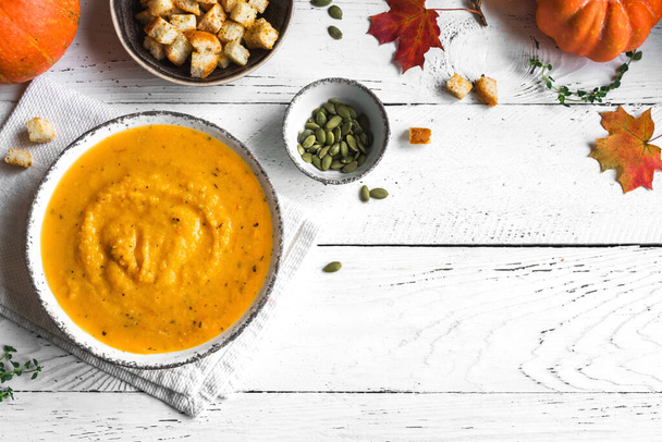 Pumpkin soup and organic pumpkins on white wooden table, top view, copy space. Seasonal autumn food - Spicy pumpkin and carrot soup. - Фото, изображение
