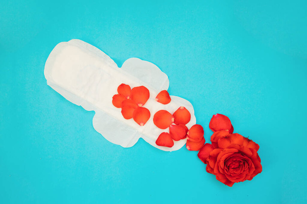 Women's padding with red rose petals on a blue background.Medical photography concept.Gynecological menstrual cycle. Women's hygiene during critical days. - 写真・画像
