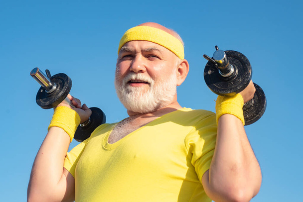 Senior sport man exercising with dumbbell. Be in motion. Grandfather sportsman portrait on blue sky backgrounds. Sport for senior man. - Photo, Image