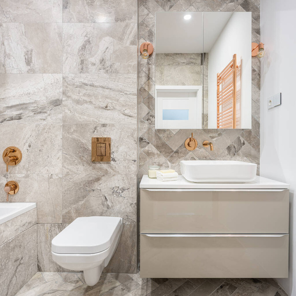 Beige bathroom with marble style tiles and copper details like taps, lamps and wall heater - Zdjęcie, obraz
