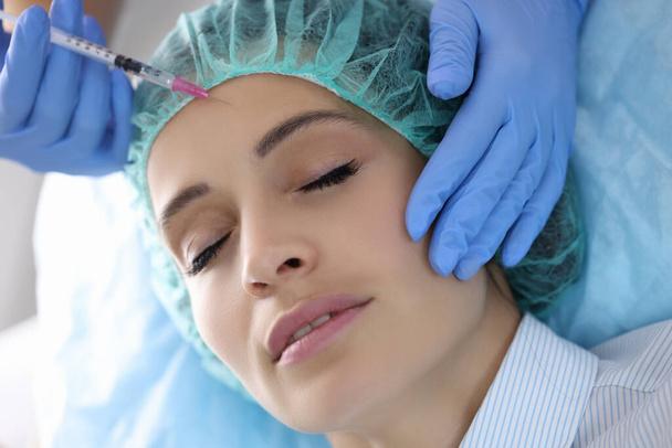 Kosmetikerin spritzt junge Frau im Schönheitssalon Spritze in die Stirn - Foto, Bild