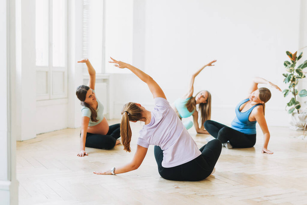 Group of pregnant women in sports uniforms with coach doing gymnastic in bright studio - Photo, Image