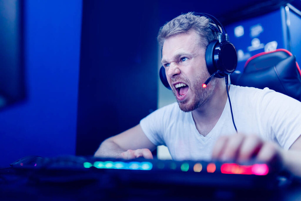 Streamer νεαρός άνδρας χαίρεται στη νίκη επαγγελματίας gamer παίζοντας online παιχνίδια υπολογιστή με ακουστικά, νέον χρώμα - Φωτογραφία, εικόνα