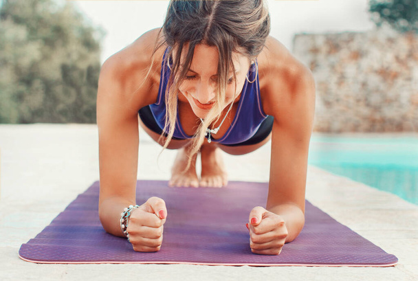 Young woman practicing elbow plank pose near a pool close up - Photo, Image