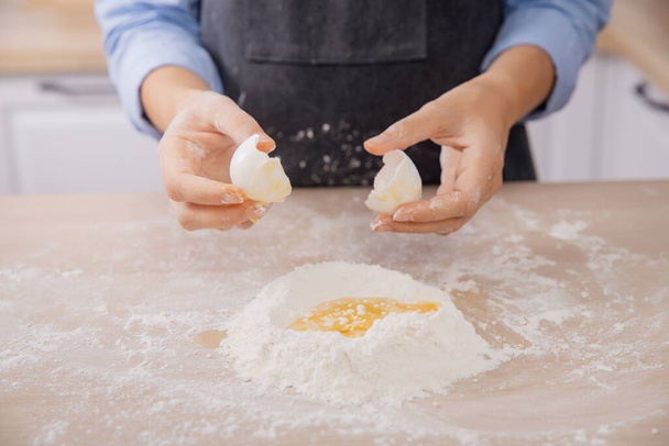 Mujer cocinero rompe el huevo en harina, amasar la masa en la cocina blanca. Fotografía en movimiento - Foto, imagen