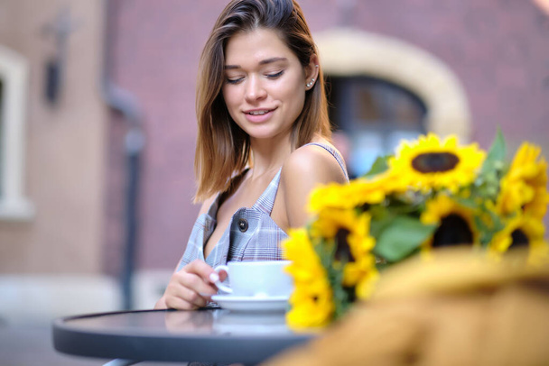 Woman drinking coffee in a cafe on the street. there is a bouquet of sunflowers on the table - Photo, Image