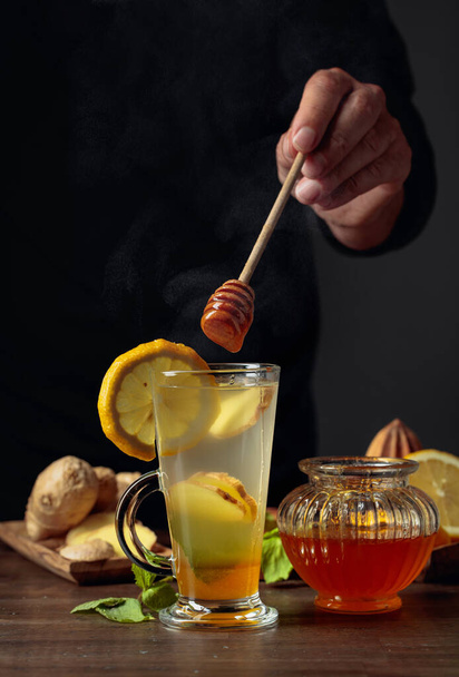 Gember thee met citroen, munt en honing. Man voegt honing toe aan thee. - Foto, afbeelding