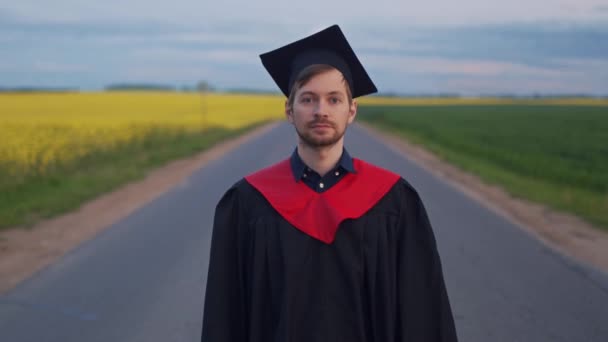 Graduado satisfecho muestra diploma de pie en la carretera - Imágenes, Vídeo