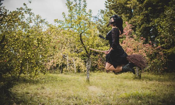 Молодая красивая и таинственная ведьма, летающая на метле в лесу. Левитация, ведьма в шляпе летит на метле, свободное место. Хэллоуин праздник, магия - Фото, изображение