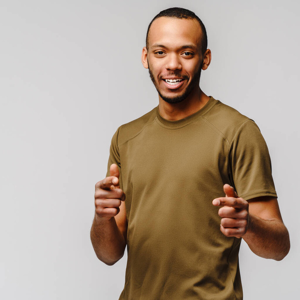 Joyful friendly african-american young man in green t-shirt over light grey background with copy space - Foto, afbeelding