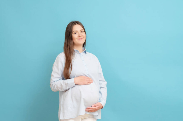 young pregnant woman on blue background in blue clothes - Foto, afbeelding