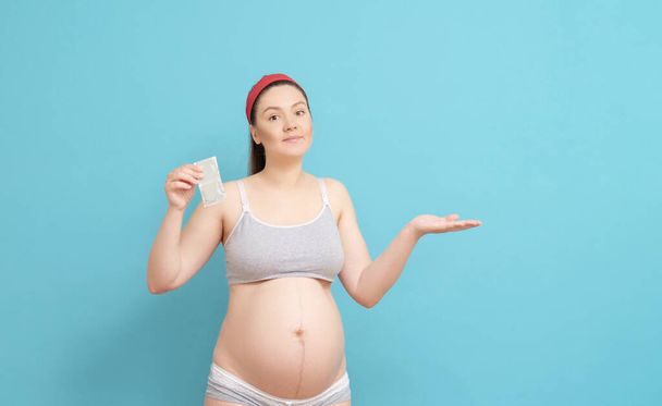 funny young pregnant woman on blue background,  holding condom in her hands - Fotó, kép