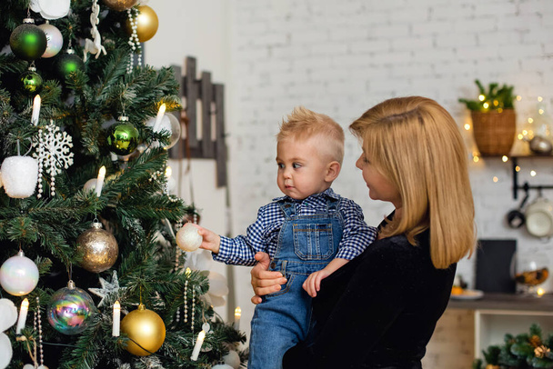 Πορτρέτο της ευτυχισμένης μητέρας και αξιολάτρευτο μωρό γιορτάζουν τα Χριστούγεννα. Πρωτοχρονιάτικες διακοπές. Βρέφος με τη μαμά στο εορταστικά διακοσμημένο δωμάτιο με χριστουγεννιάτικο δέντρο και διακοσμήσεις. - Φωτογραφία, εικόνα