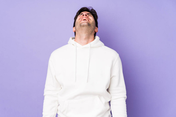 Young man isolated on purple background relaxed and happy laughing, neck stretched showing teeth. - Zdjęcie, obraz