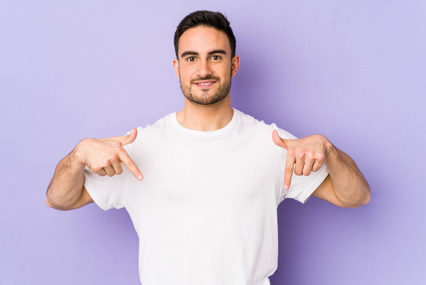 Young caucasian man isolated on purple background points down with fingers, positive feeling. - Foto, afbeelding