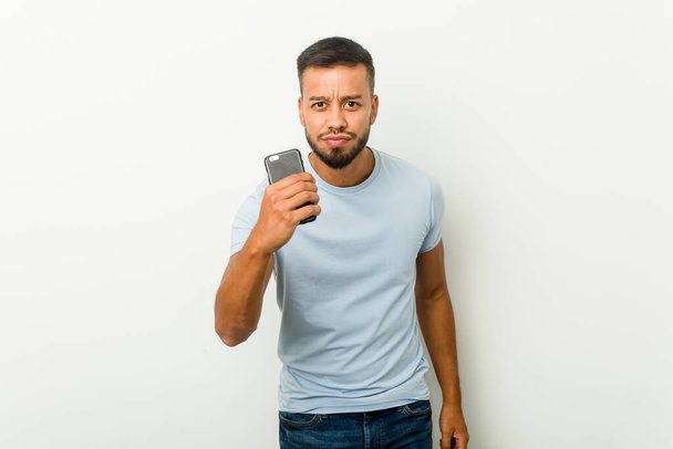 Young mixed race asian man holding a phone showing fist to camera, aggressive facial expression. - Photo, image