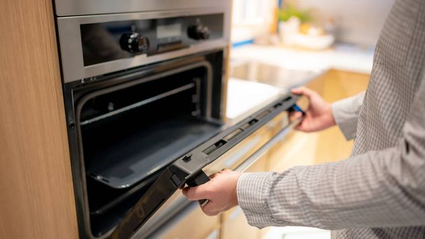 Male hand opening oven door in the kitchen showroom. Buying cooking appliance for domestic kitchen. Home improvement concept - Photo, Image