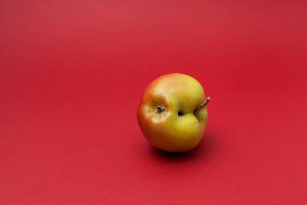 Ugly apple with flaws on a red background. Selective focus, copy space. Concept - Food waste reduction. Using in cooking imperfect products. - Фото, зображення
