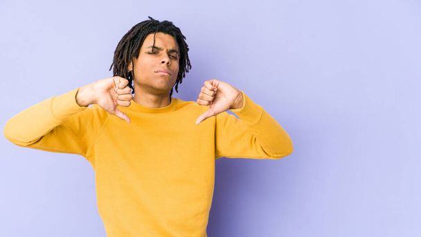 Jonge zwarte man draagt rasta kapsel tonen duim naar beneden, teleurstelling concept. - Foto, afbeelding