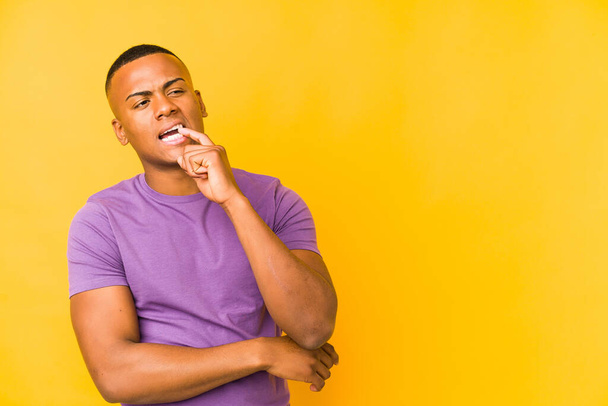 Young latin man isolated on yellow background relaxed thinking about something looking at a copy space. - Photo, Image