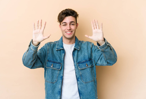 Giovane uomo caucasico isolato su sfondo beige mostrando il numero dieci con le mani. - Foto, immagini