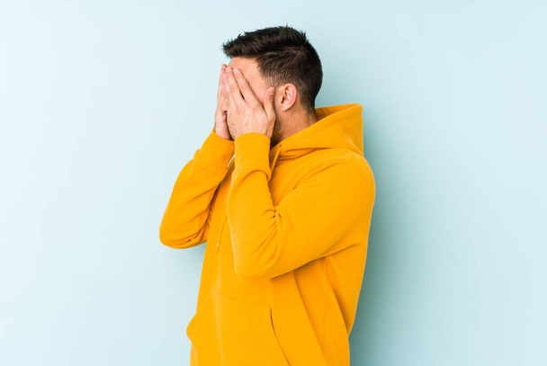 Young caucasian man isolated on blue background afraid covering eyes with hands. - Foto, afbeelding