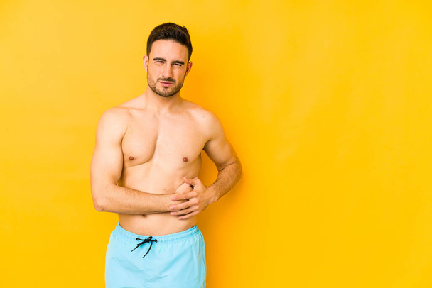 Junger kaukasischer Mann mit Badeanzug isoliert auf gelbem Hintergrund Junger kaukasischer Mann mit Leberschmerzen, Bauchschmerzen. - Foto, Bild