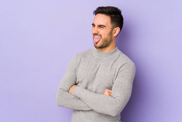 Young caucasian man isolated on purple background funny and friendly sticking out tongue. - Photo, Image