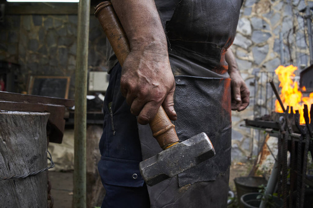 Großaufnahme einer Schmiedehand, die einen Hammer hält. Der Besitzer und Arbeiter einer kleinen Schmiede, der in seinem Beruf arbeitet. Die Hand ist schmutzig, weil sie funktioniert hat. - Foto, Bild