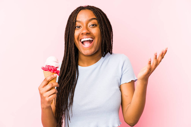 若いアフリカ系アメリカ人の女性が手を上げ興奮し、快適な驚きを受けて隔離されたアイスクリームを保持. - 写真・画像